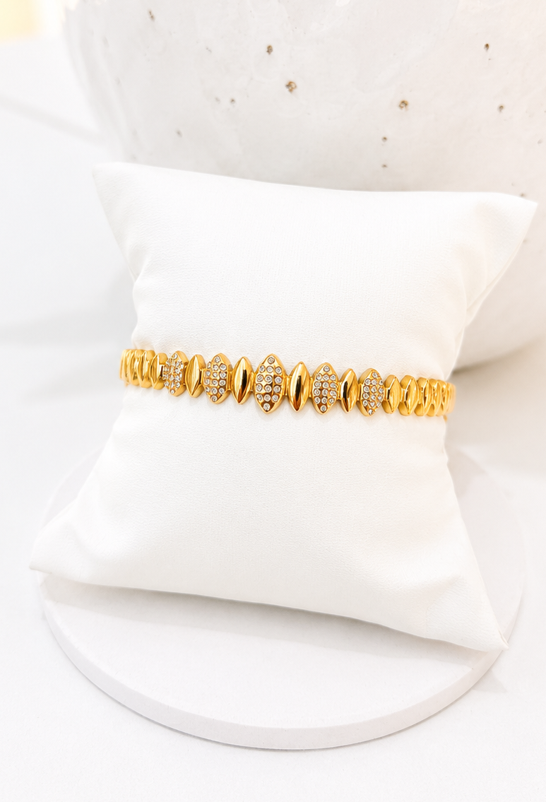 
                  
                    A gold Cubic Zirconia bracelet displayed on a white satin pillow, with a white textured ceramic vase in the background.
                  
                