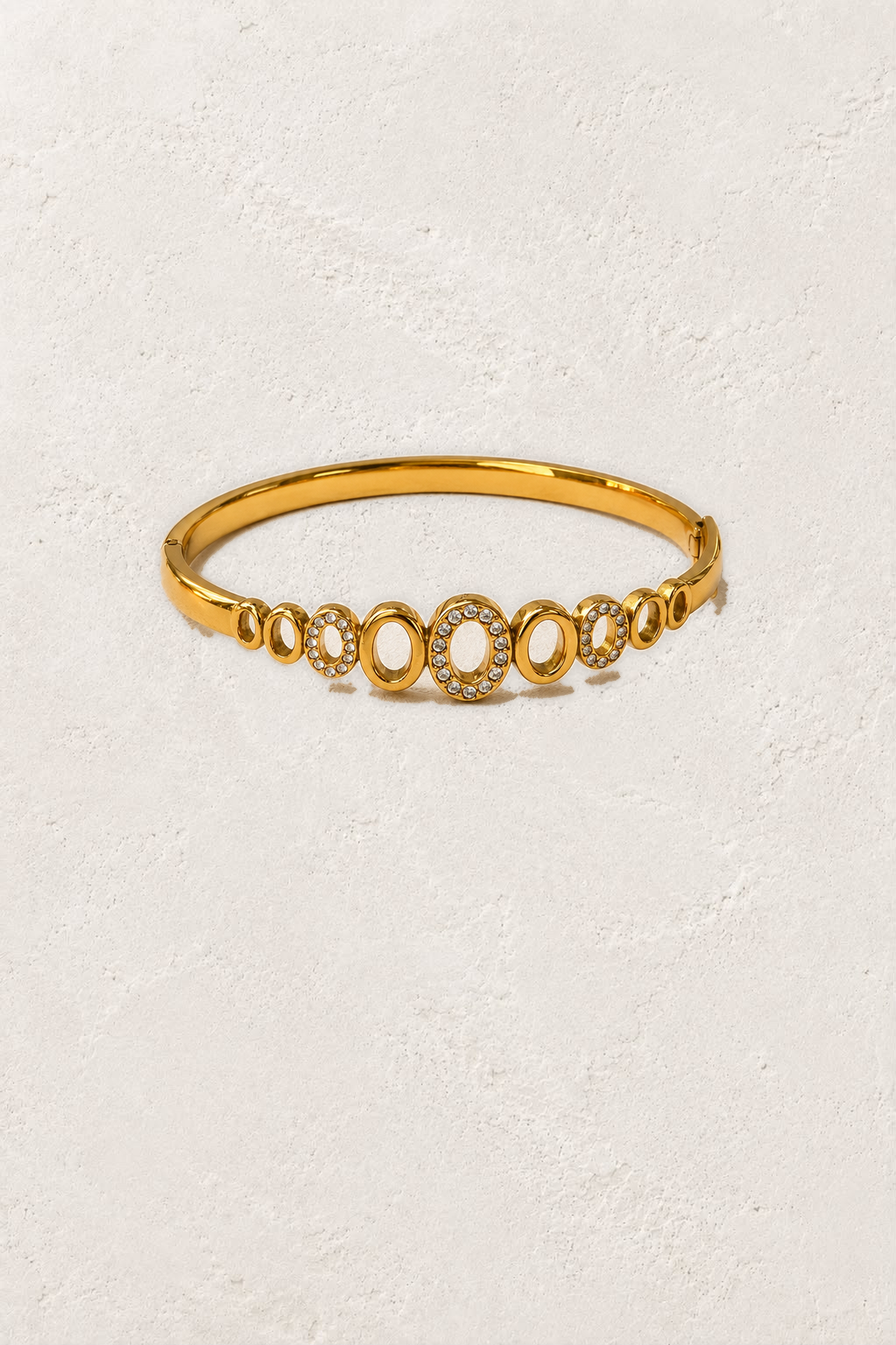 Amoura Open Oval Gold Crystal Bangle on the reference plaster background