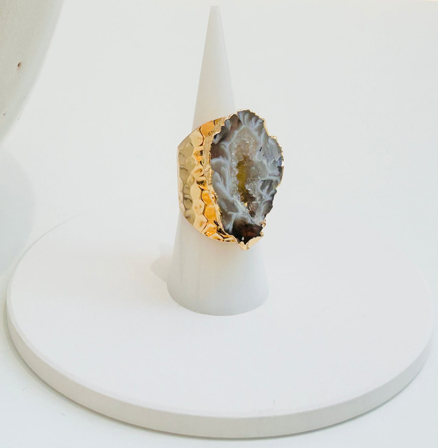 
                  
                    A gold ring with a large natural agate geode slice setting, displayed on a white cone stand against a white background.
                  
                