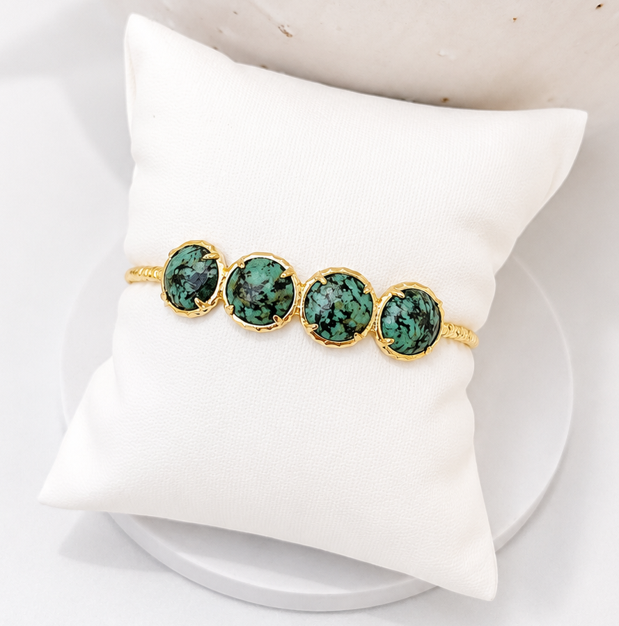 
                  
                    Gold ring with African Turquoise gemstones on a white pillow against a neutral background
                  
                