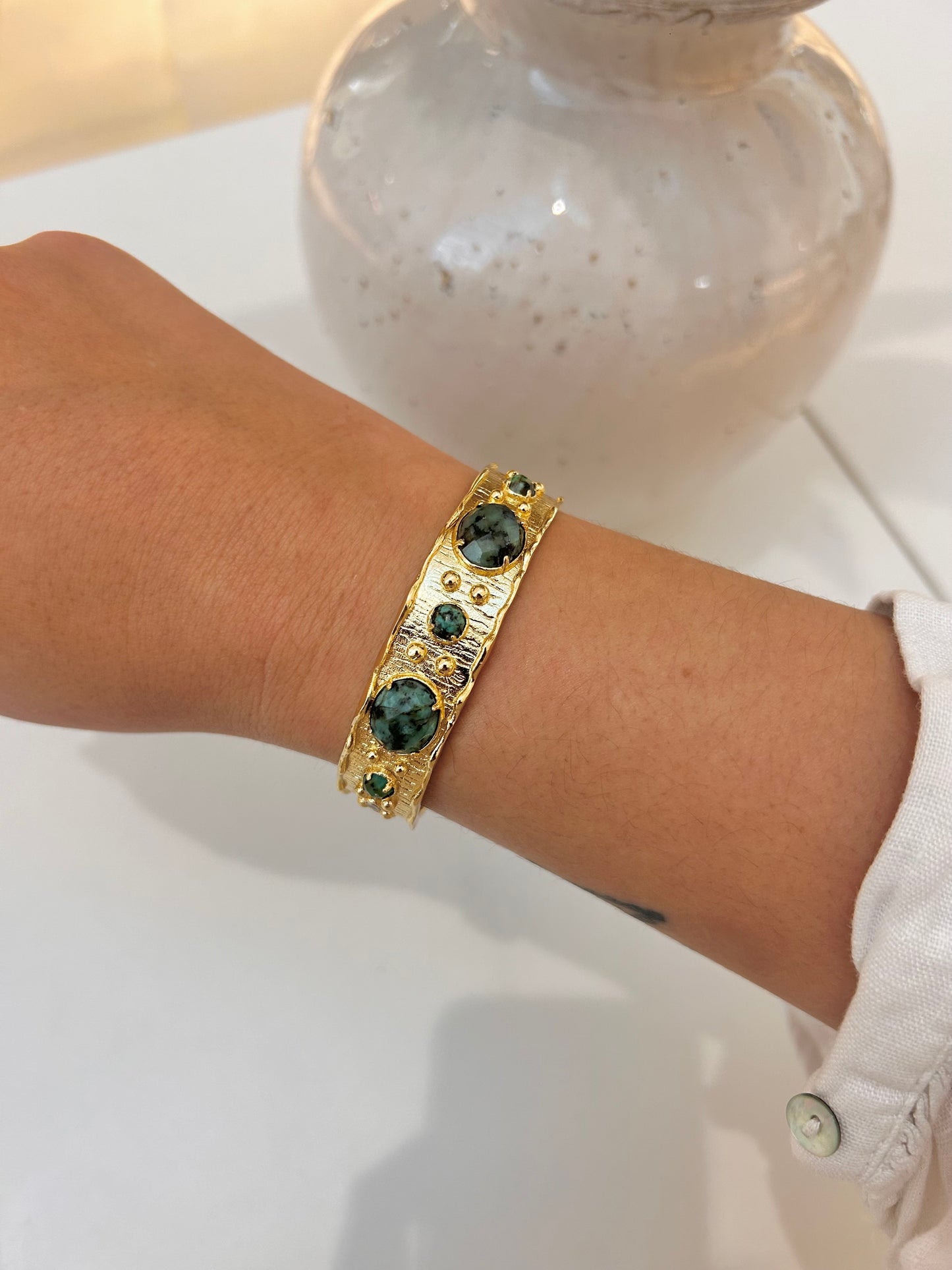 A gold-toned cuff bracelet with African turquoise gemstone accents, worn on a person's wrist.