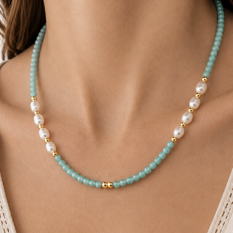 A close-up of a model wearing a delicate necklace featuring light amazonite blue-green beads, white pearls, and small gold spacer beads, styled with a cream-colored lace-trimmed top.
