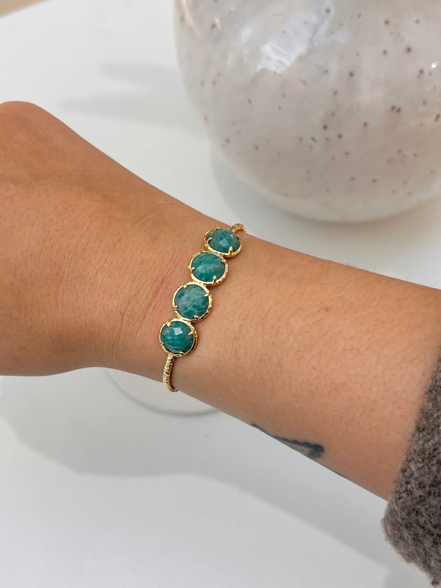 A gold-plated bracelet with four round amazonite stones, worn on a person's wrist.