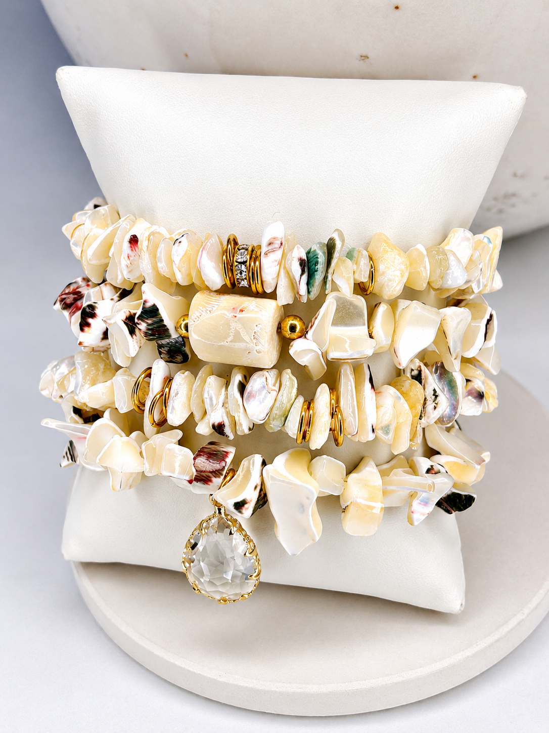 
                  
                    Stack of shell bracelets on a white surface with a neutral background
                  
                