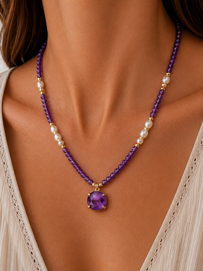 A close-up of a model wearing a beaded necklace with amethyst beads, white pearl-like accents, and a round purple gemstone pendant in gold-toned settings.