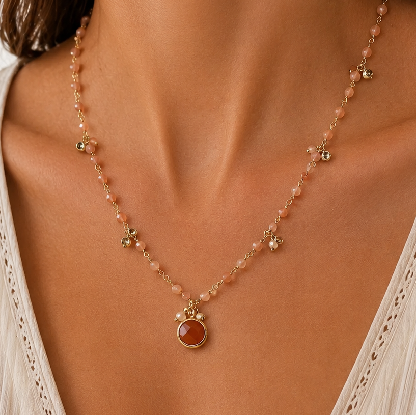 A close-up of a model wearing a delicate gold-toned beaded necklace with a central round sunstone pendant, cubic zirconia pendants paired with a cream-colored lace-trim V-neck top.