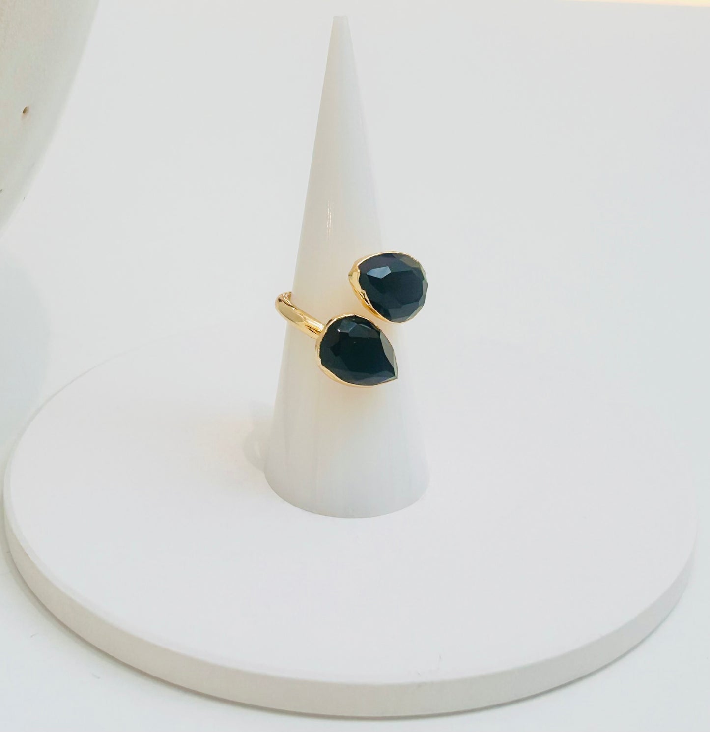 
                  
                    A gold ring with two faceted dark black obsidian teardrop gemstones, displayed on a white cone jewellery stand against a white background.
                  
                