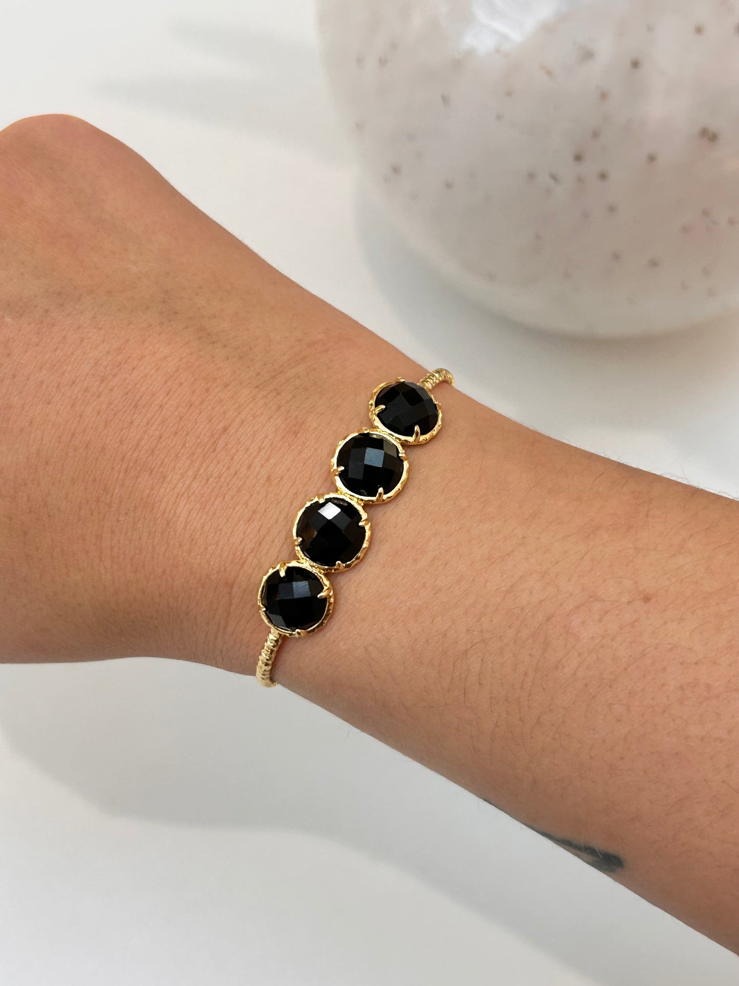 A gold-toned bracelet with four round black obsidian natural gemstones, shown worn on a person's wrist against a light background.