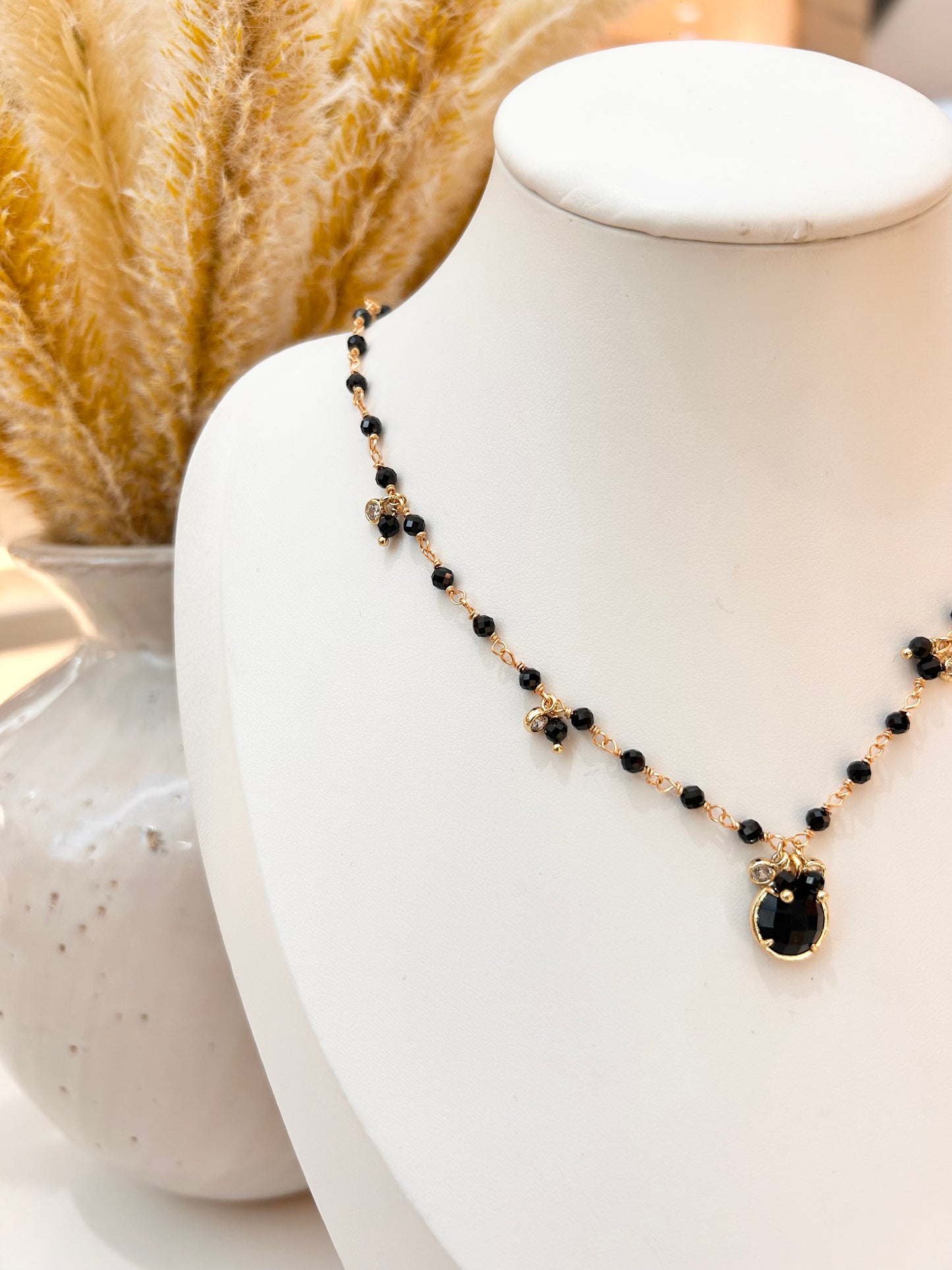 
                  
                    A delicate necklace with small black beads and gold-toned accents, featuring a black obsidian stone pendant, displayed on a white jewelry bust.
                  
                