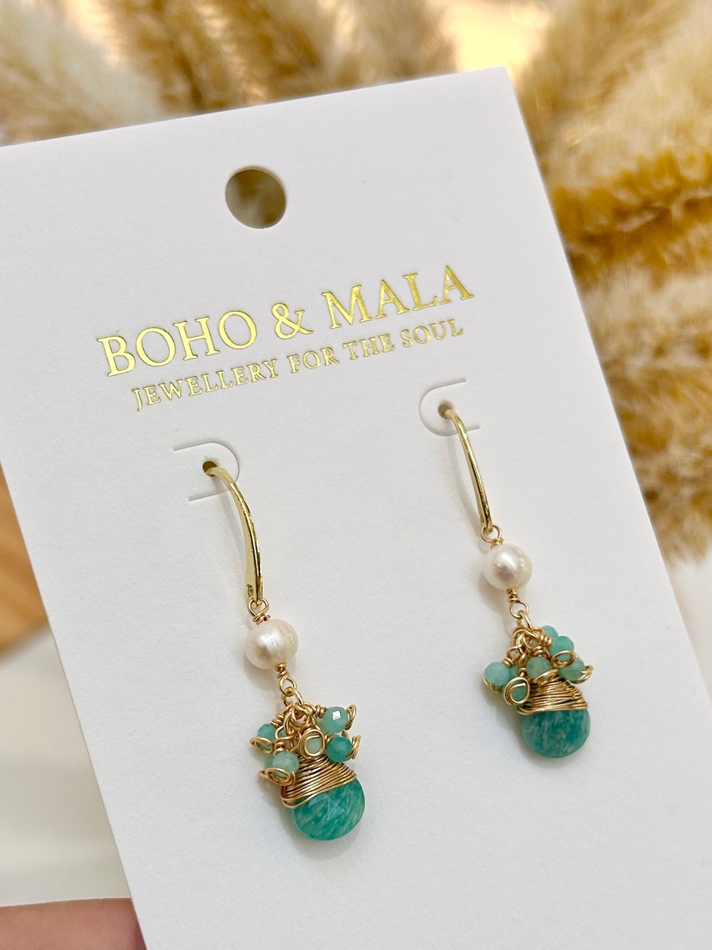 
                  
                    Pair of earrings on a 'Boho & Maia' branded card held by a hand.
                  
                