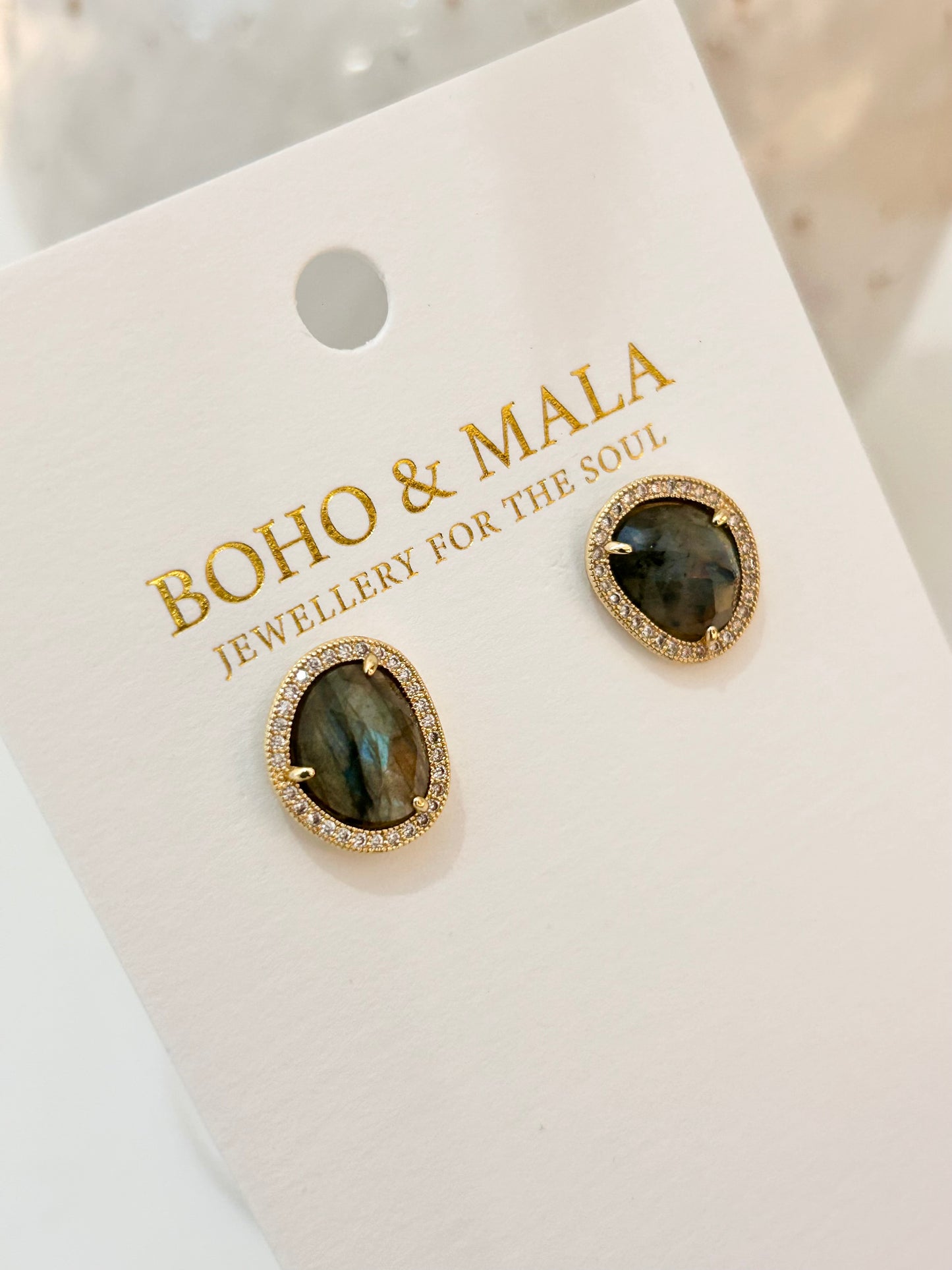
                  
                    Gold earrings with labradorite stones on a 'Boho & Mala' branded card.
                  
                