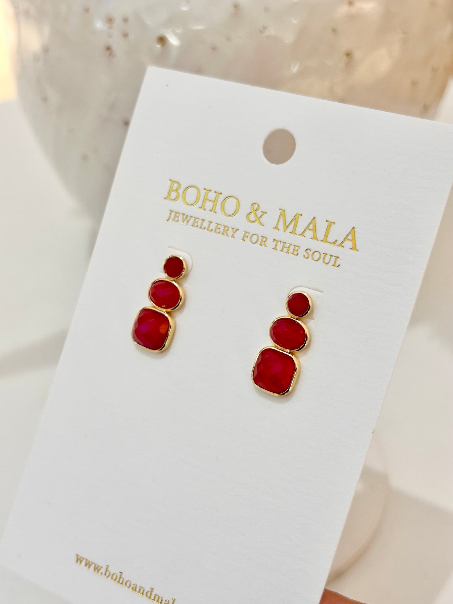 
                  
                    Red earrings on a 'Boho & Mala' branded card with a blurred background
                  
                