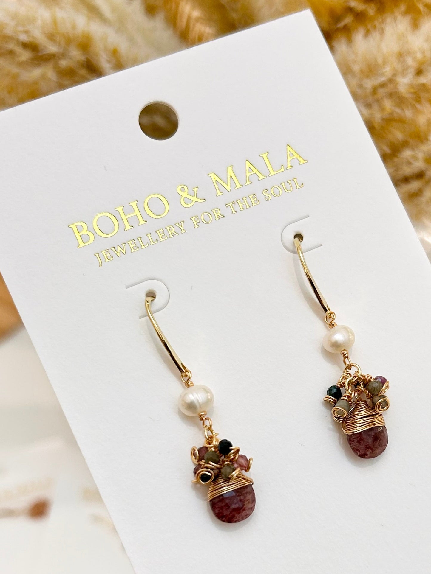 
                  
                    Pair of earrings on a BOHO & MALA card held by a hand with dark nail polish.
                  
                