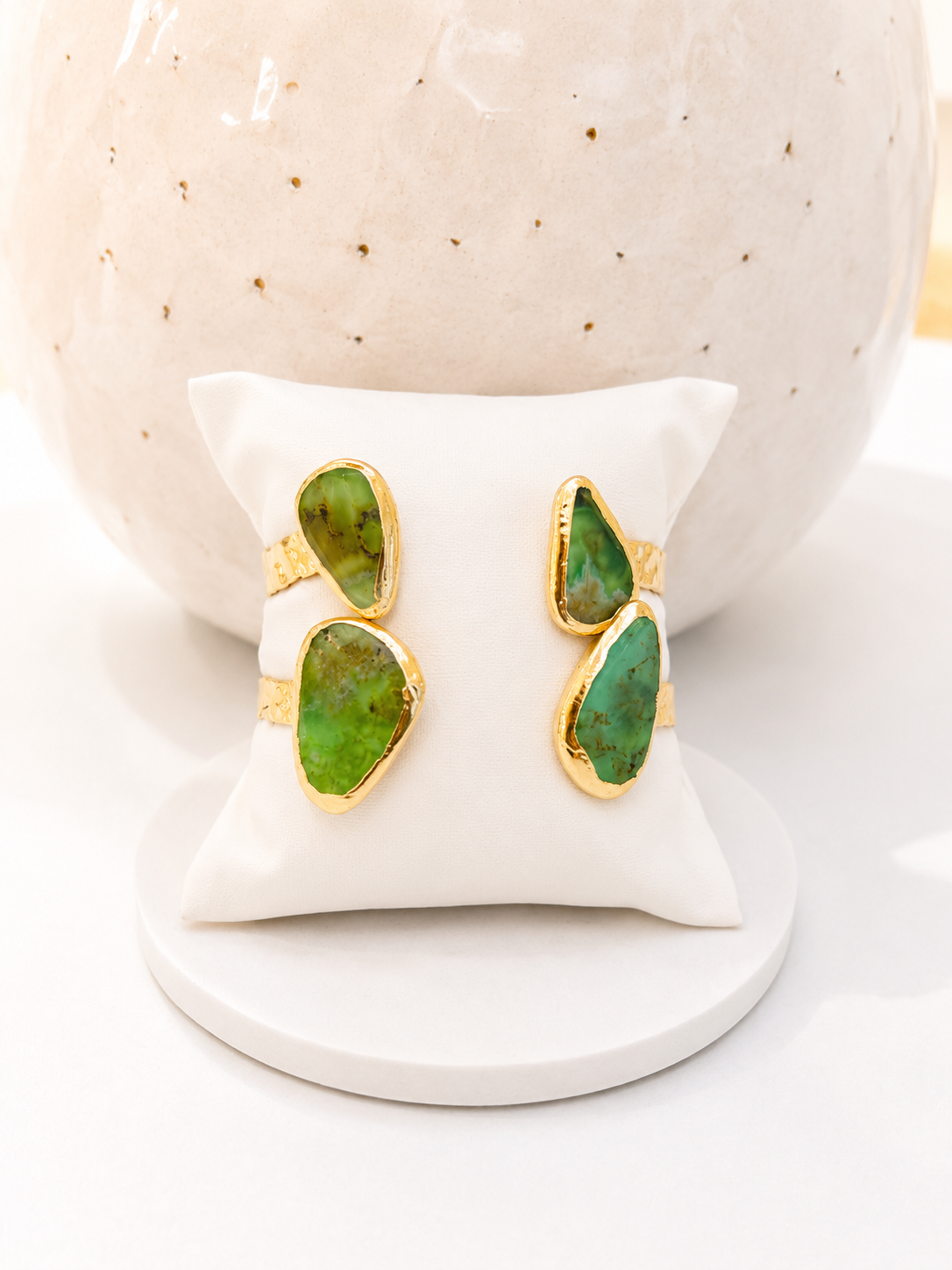 
                  
                    Gold-plated open cuff bracelet featuring two natural Chrysoprase stones in organic freeform shapes, displayed on a white jewellery stand.
                  
                