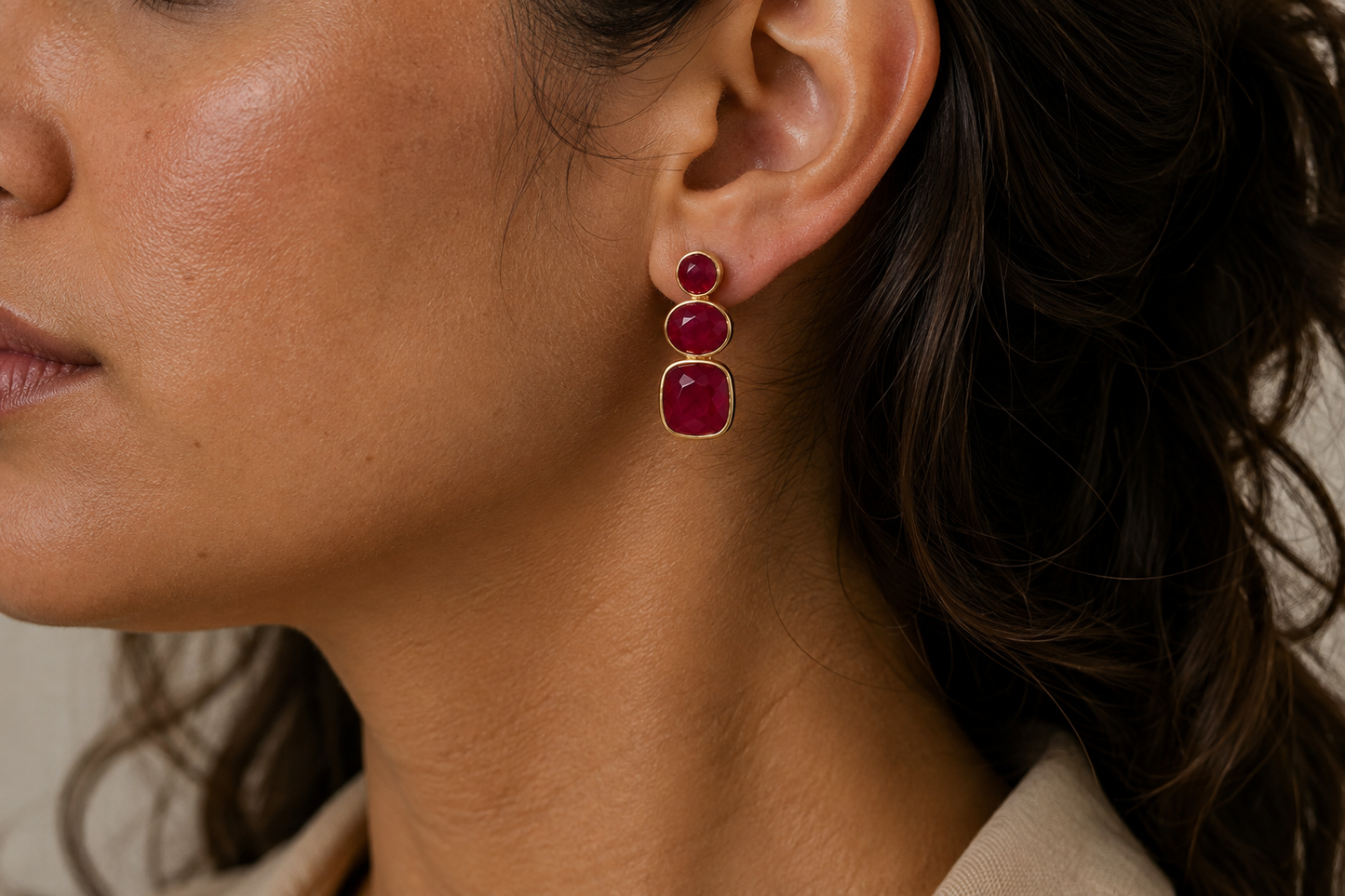 A close-up of a model's ear wearing a gold drop earring with two stacked oval deep red jade gemstones.