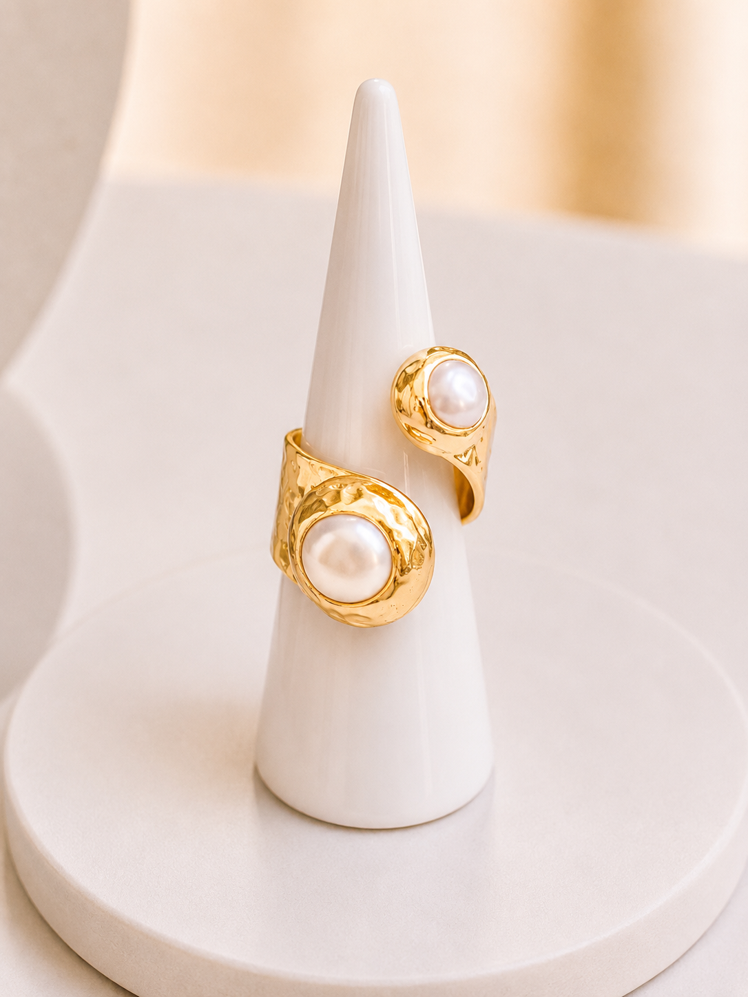 gold ring with large white freshwater pearls, displayed on a white cone stand against a soft beige background.