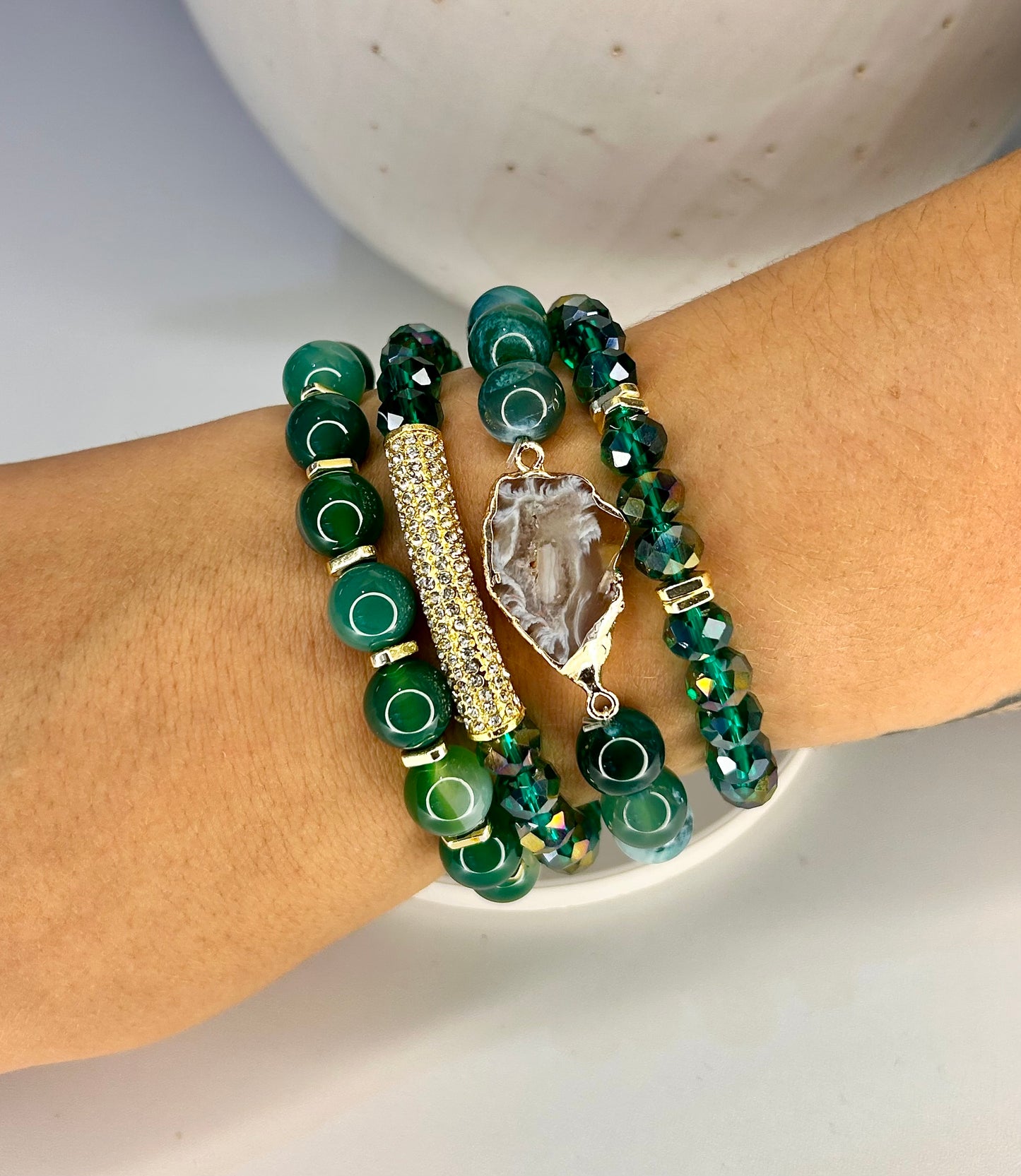 Stack of green beaded natural stone bracelets on a wrist with a neutral background