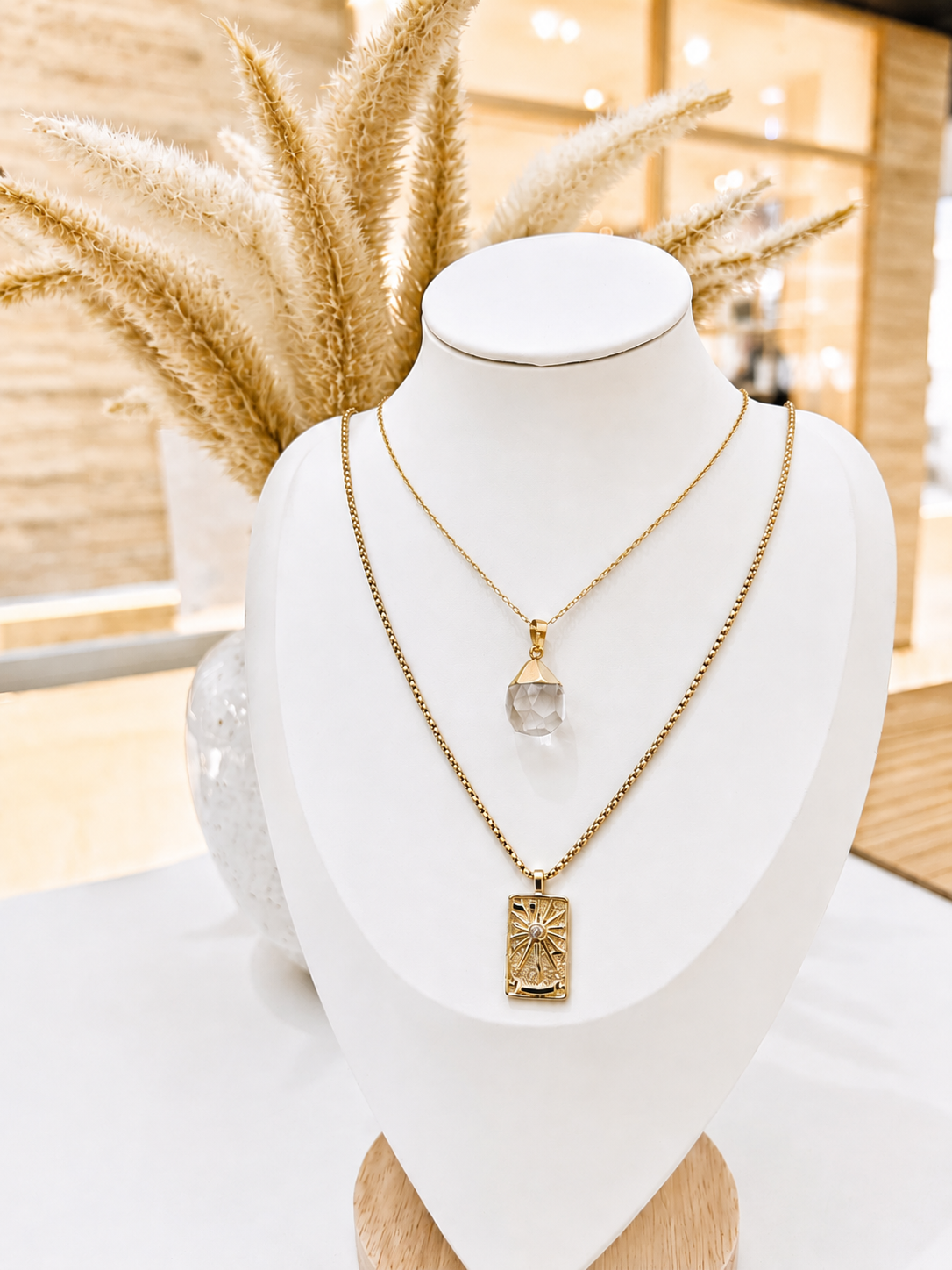 Gold necklace with a pendant on a mannequin bust against a blurred indoor background
