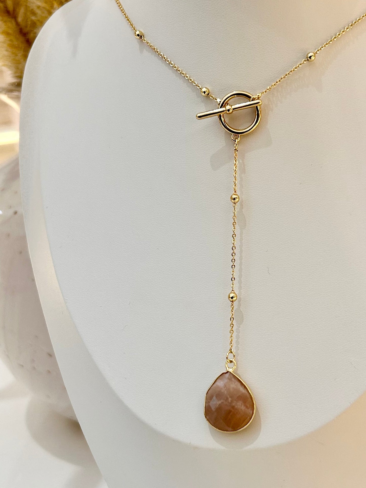 
                  
                    Gold necklace with a teardrop-shaped sunstone pendant on a mannequin bust.
                  
                