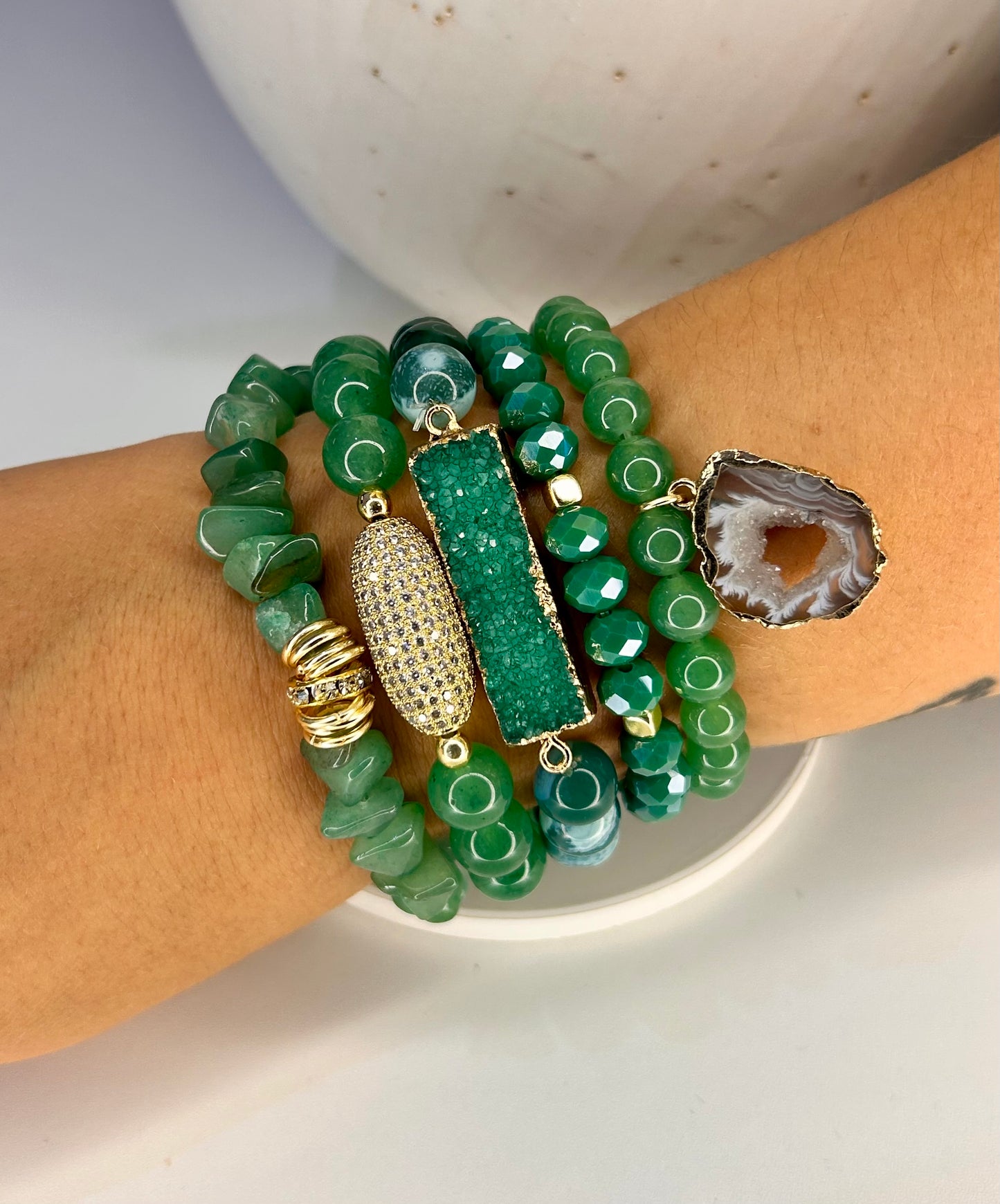 Green beaded natural stone bracelets with gold accents on a wrist against a neutral background