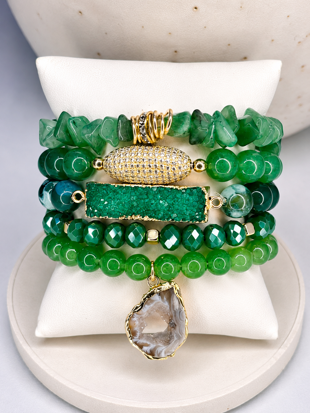 Stack of green natural stone beaded bracelets with gold accents on a white surface