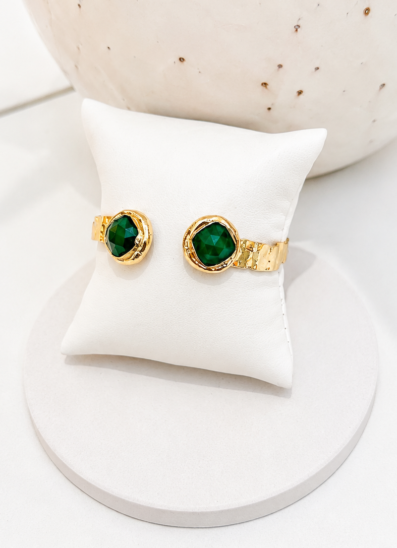 
                  
                    Gold plated cuff bangles with round green jade gemstones, displayed on a white cushion atop a round white stand.
                  
                