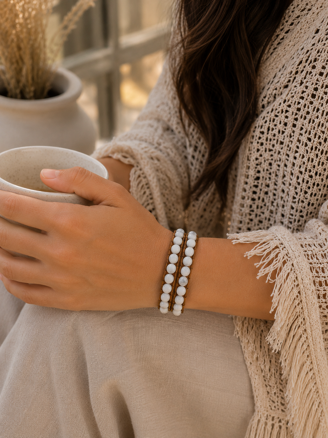 
                  
                    Person holding a mug with a focus on a wrap howlit  bracelet, wearing a beige sweater.
                  
                
