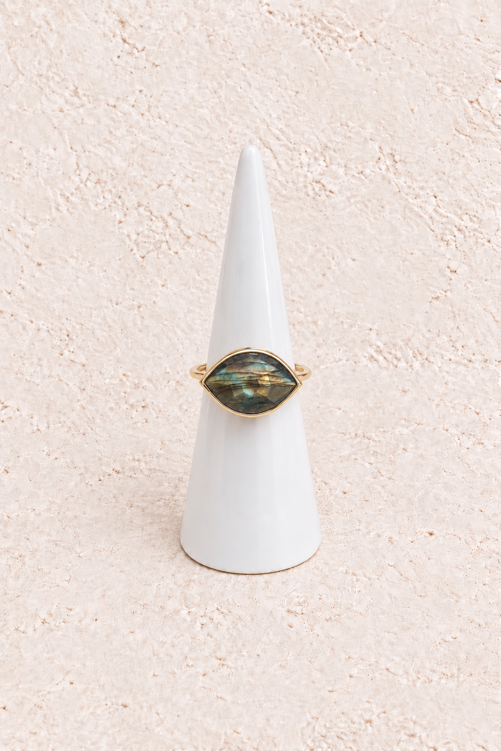 Aylin Labradorite Eye Ring on a white cone against a warm textured background