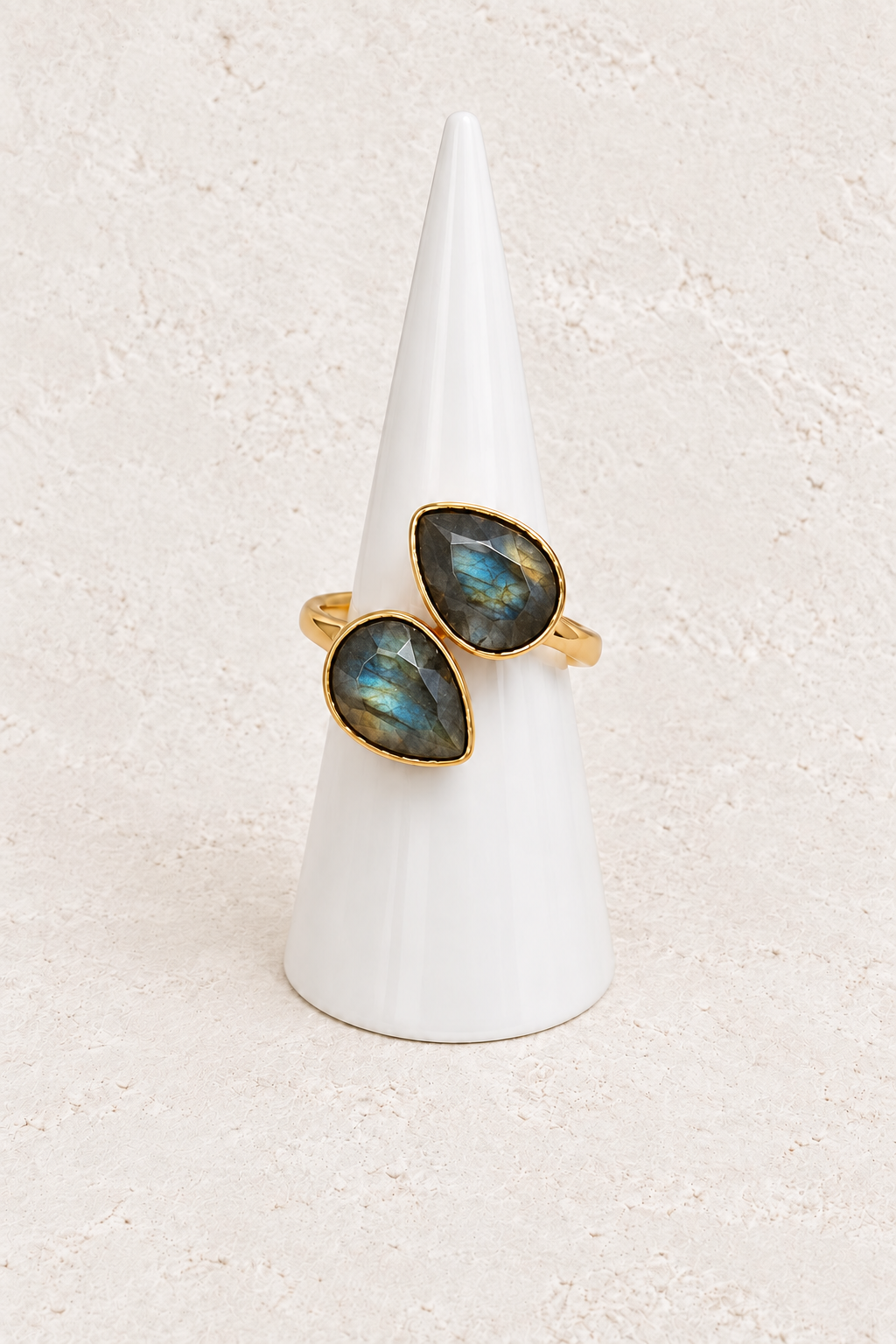 Esme Labradorite Adjustable Ring with two teardrop stones on a white cone against a warm textured background
