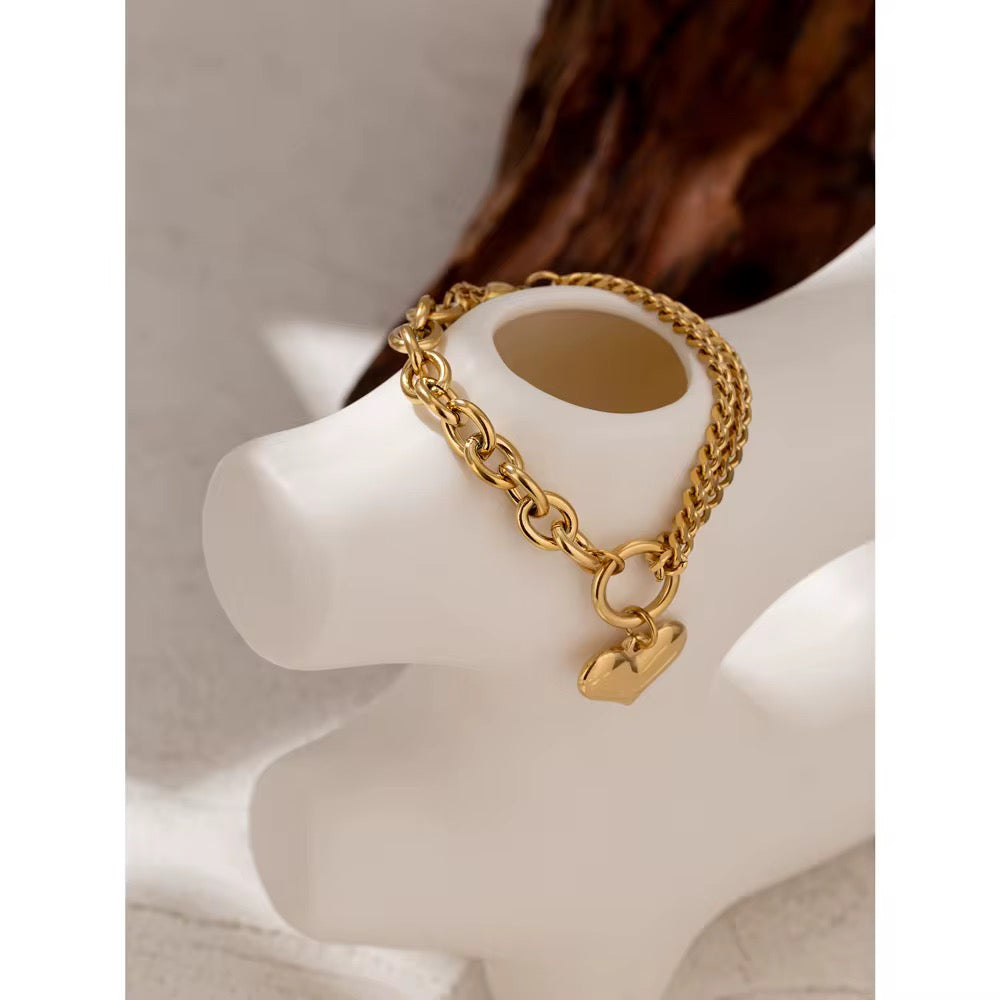 
                  
                    Golden Heart Statement Chain Bracelet displayed on a white stand
                  
                