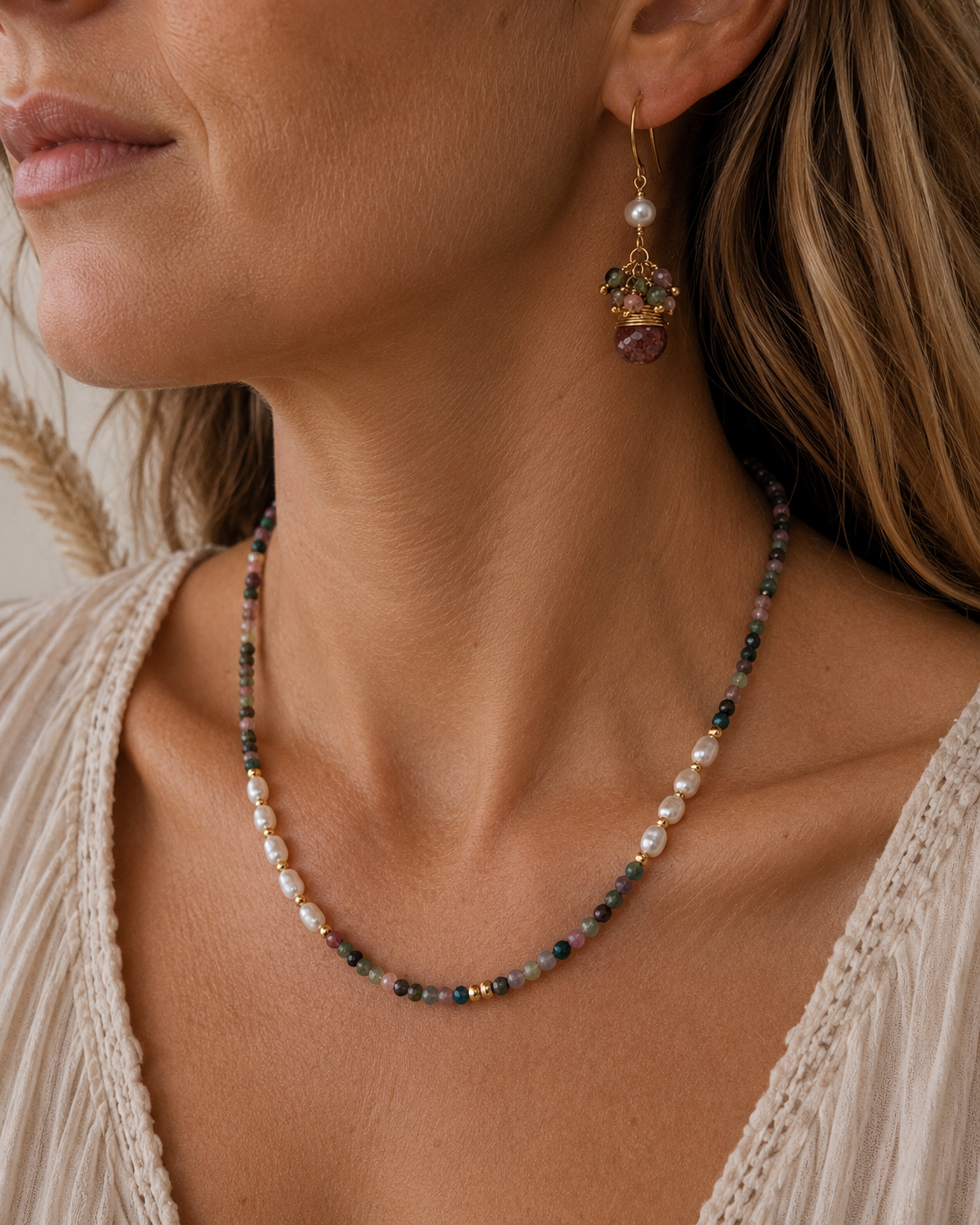 
                  
                    A close-up lifestyle shot of a woman wearing a delicate beaded necklace and matching drop earrings. The jewelry features white pearls, small multicolored beads, and gold-toned metal settings with green and purple gemstone accents.
                  
                
