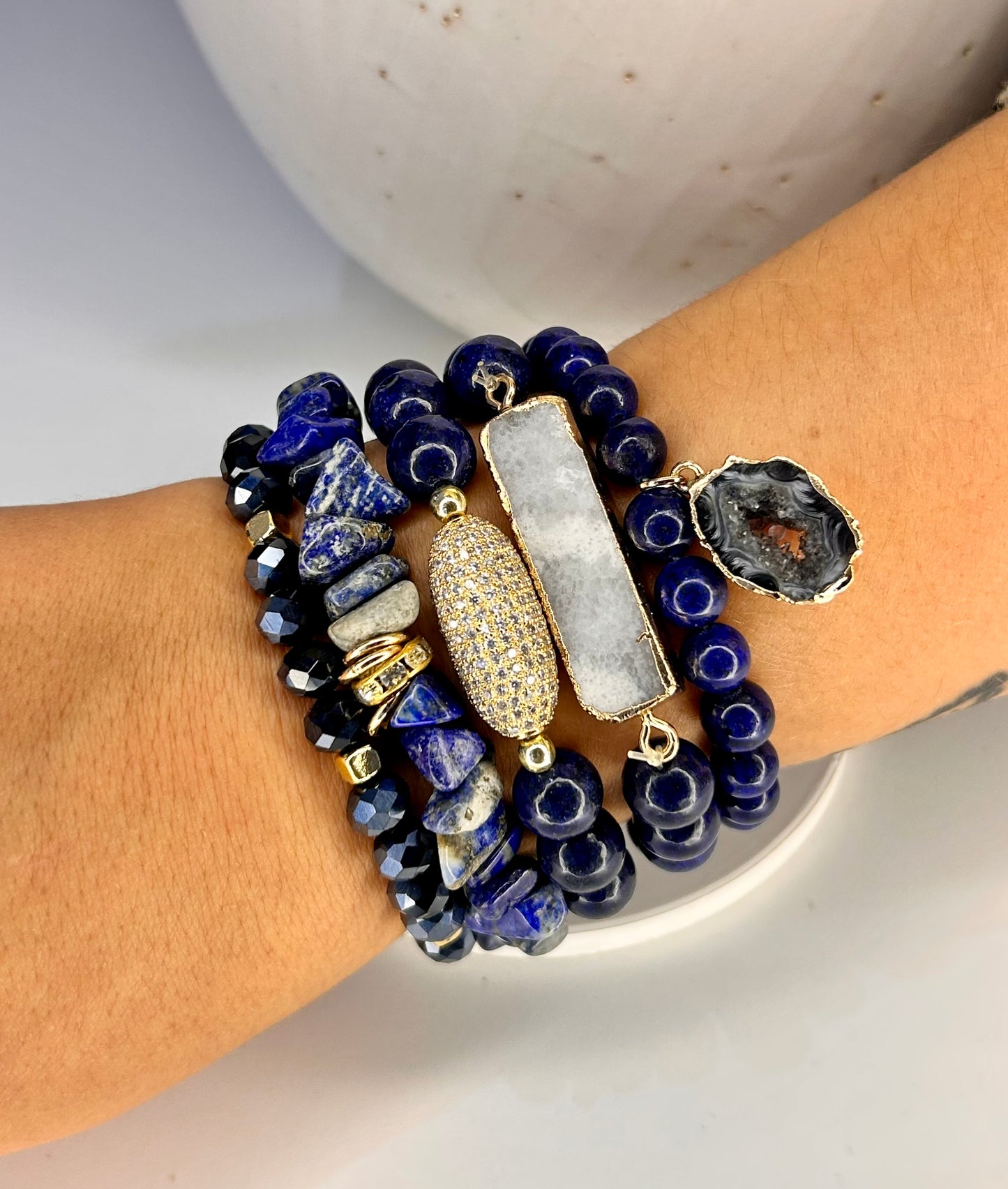 Stack of blue lapis lazuli beaded bracelets with gold accents on a wrist against a neutral background