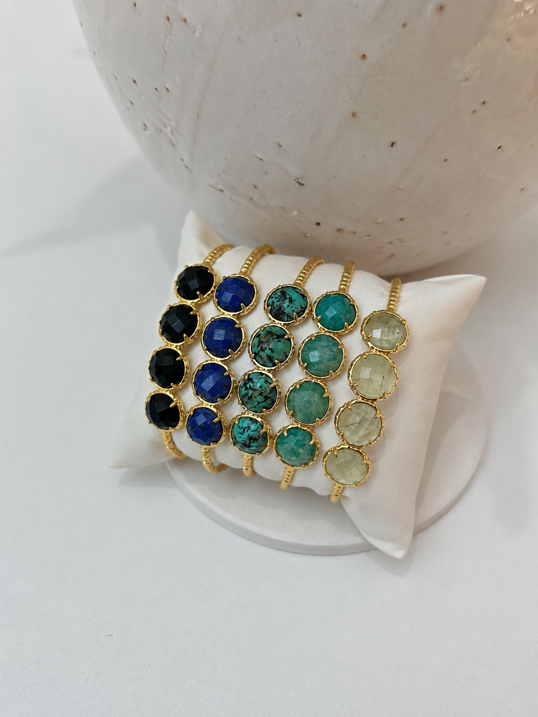 
                  
                    Bracelet with multicolored natural gemstones on a white stand against a neutral background
                  
                