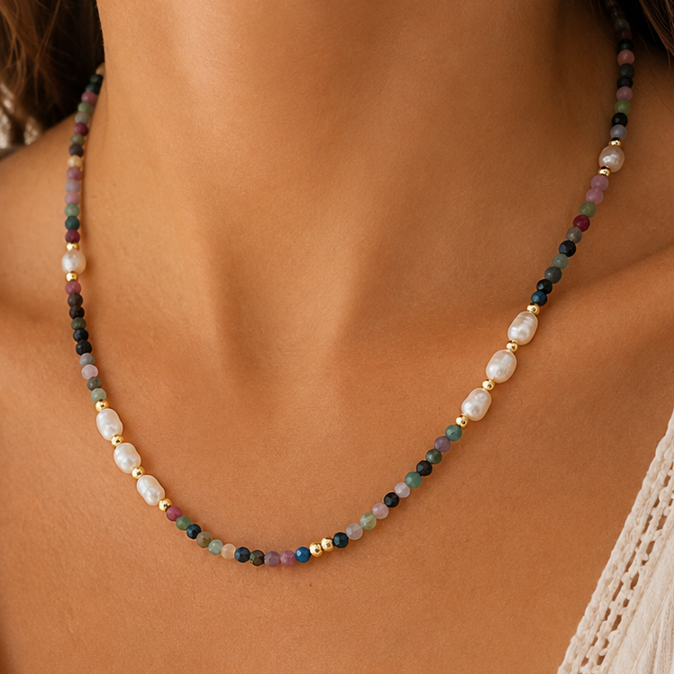 A close-up of a woman's neck and chest wearing a delicate strawberry quartz mixed beaded necklace with white pearls and small multicolored beads, paired with a cream lace-trim V-neck top.