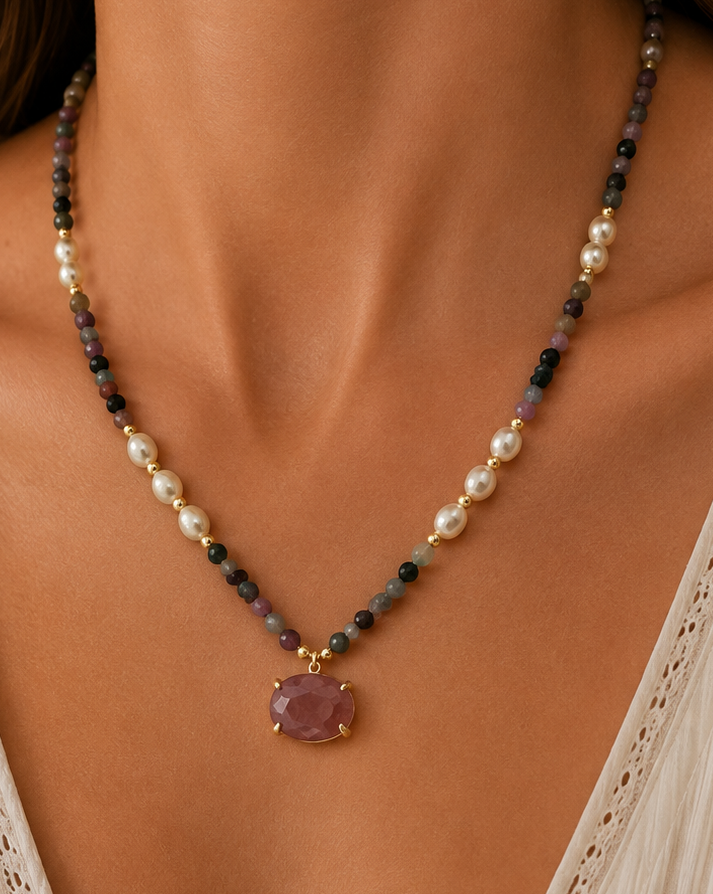 A close-up of a woman wearing a delicate mixed straweberry quartz beaded necklace with a lavender-purple pendant, styled with a cream-colored lace-trimmed top.