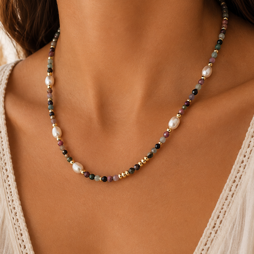 A close-up of a woman wearing a delicate beaded necklace with white pearls and small mixed sunstone beads, paired with a cream lace-trim V-neck top.