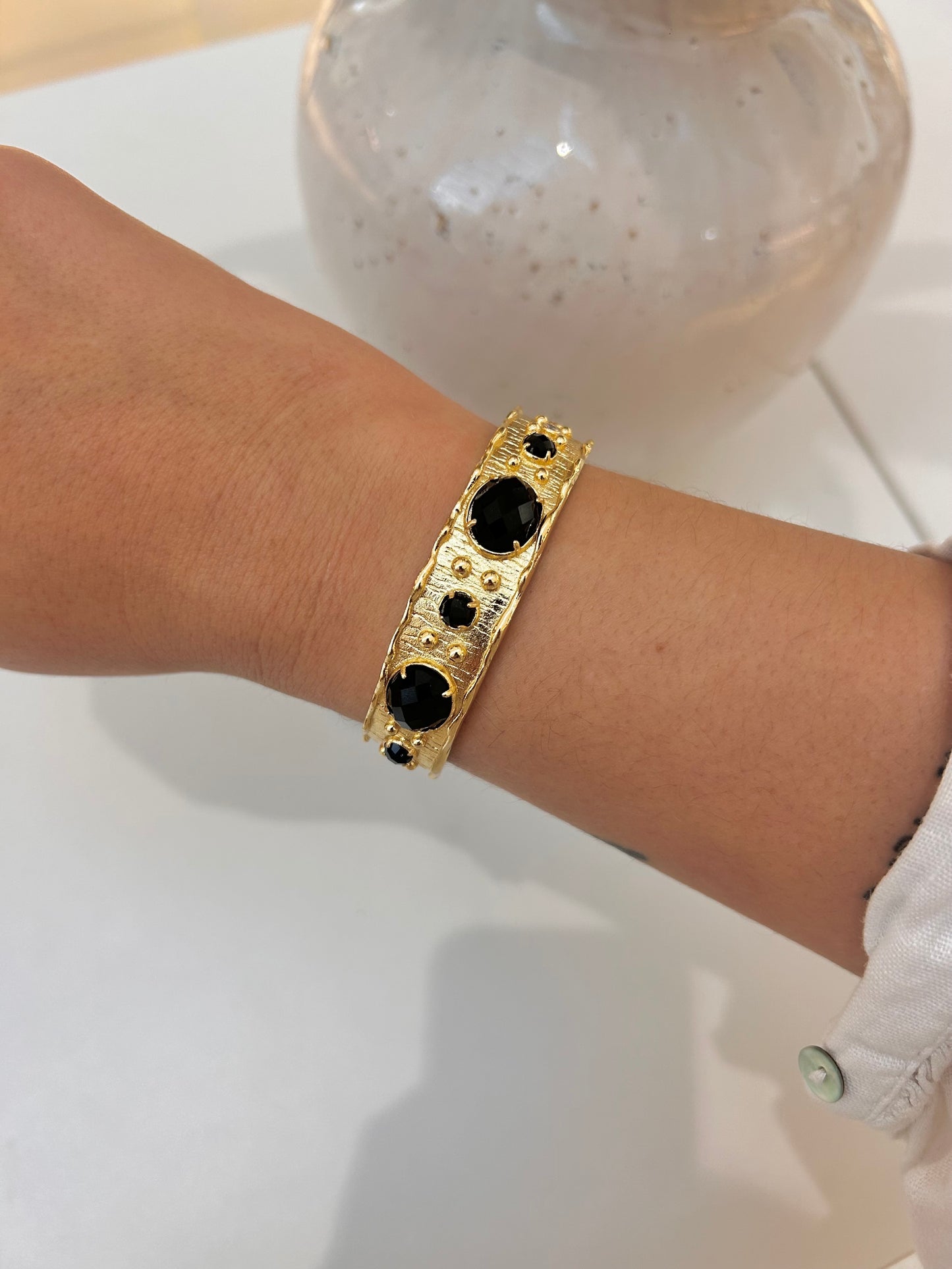 A gold-toned cuff bracelet with black obsidian stone accents, shown worn on a person's wrist.