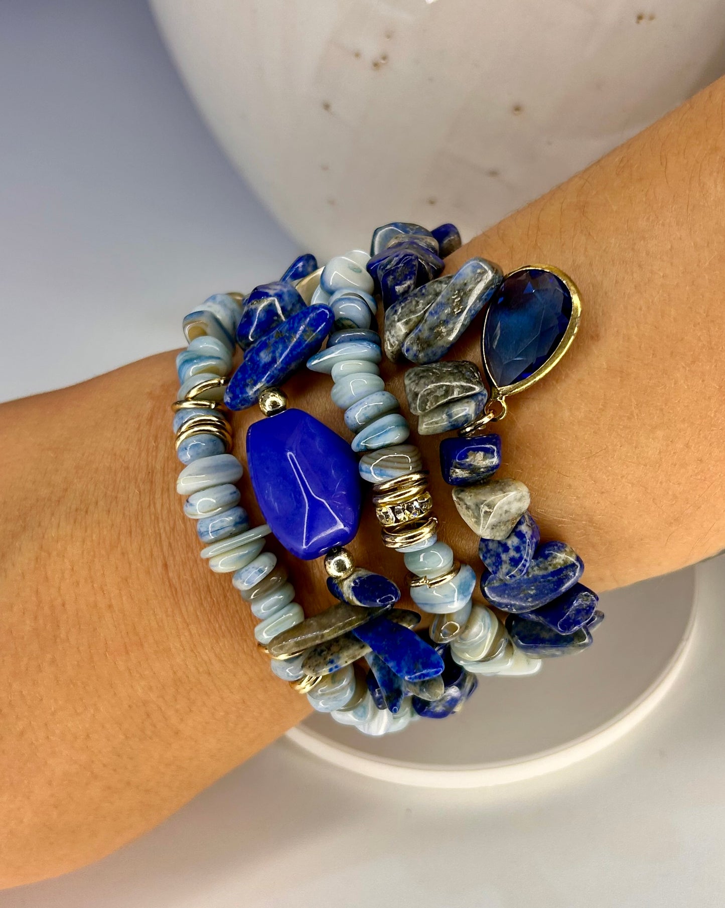 Stack of blue and gold beaded bracelets on a wrist against a neutral background with a mix of lapis lazuli stones