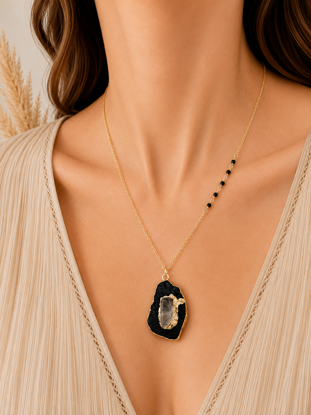 A close-up of a model wearing a delicate gold chain necklace with a black geode-style pendant and a small black bead accent on the side.