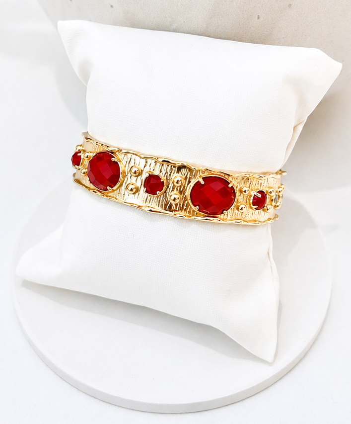 
                  
                    A gold-toned cuff bracelet with red jade gemstones, displayed on a white fabric jewellery pillow against a white background.
                  
                