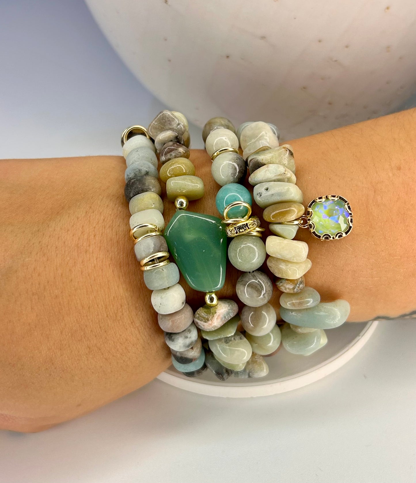 Stack of beaded green stone bracelets on a wrist with a neutral background