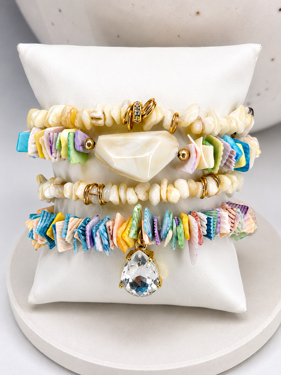 Colorful shell beaded bracelets on a white stand with a neutral background