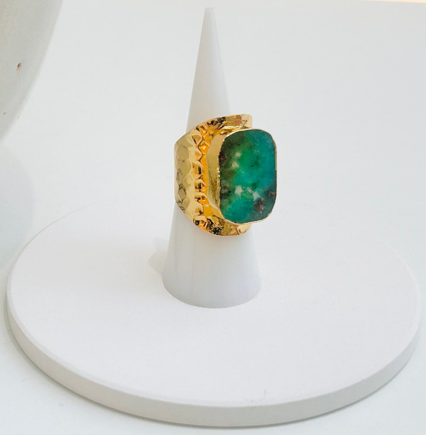 
                  
                    A gold ring with a large, textured green chrysoprase stone, displayed on a white cone stand against a white background.
                  
                