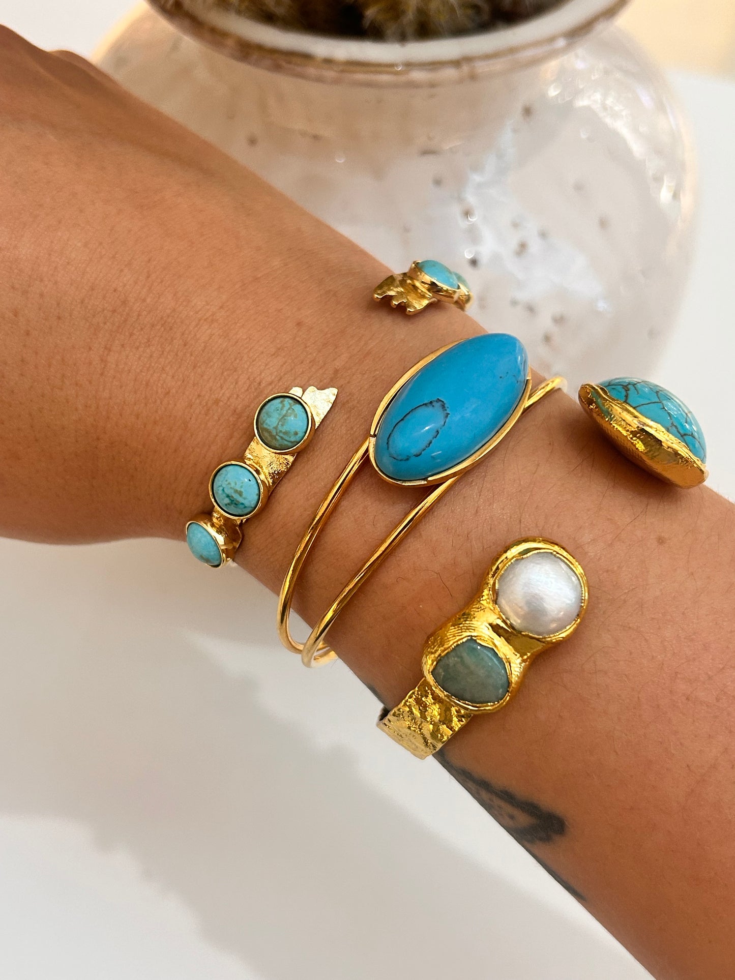Gold and turquoise bracelets on a wrist with a blurred background, stacked with different style natural stone bangles 
