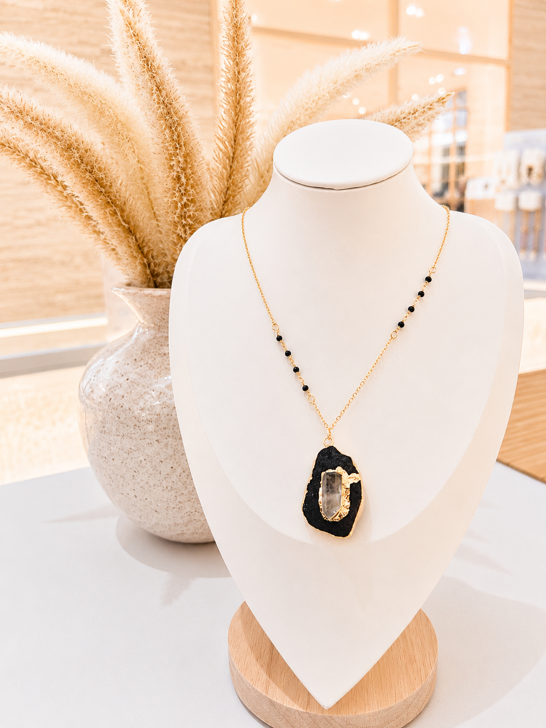 A gold necklace with a black agate slice pendant and small black beads, displayed on a white jewelry bust.