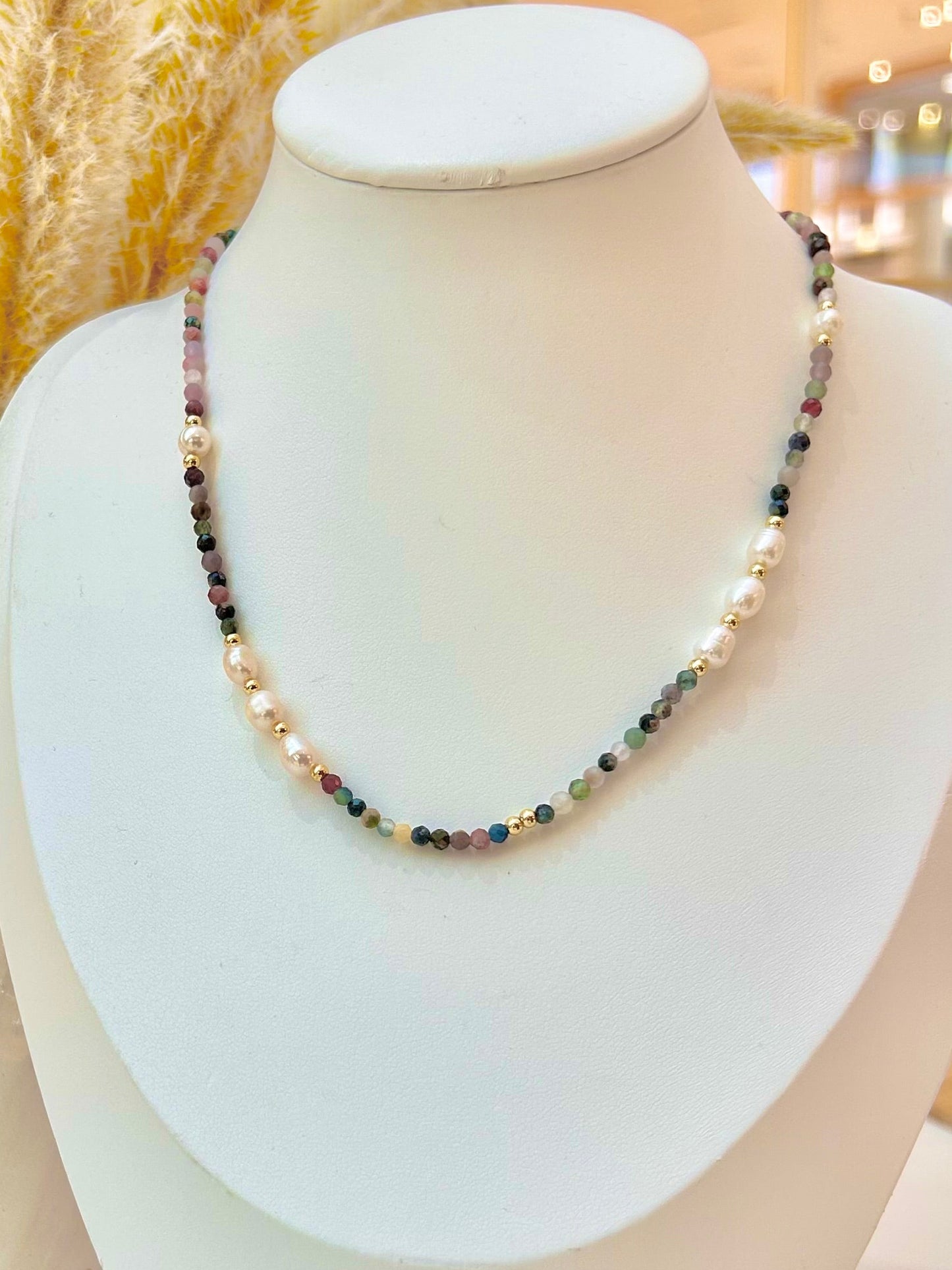 
                  
                    A beaded necklace displayed on a white jewellery bust. The necklace features alternating strands of small multicolored mixed strawberry quartz stone beads and white pearl beads, with small gold spacer beads throughout.
                  
                