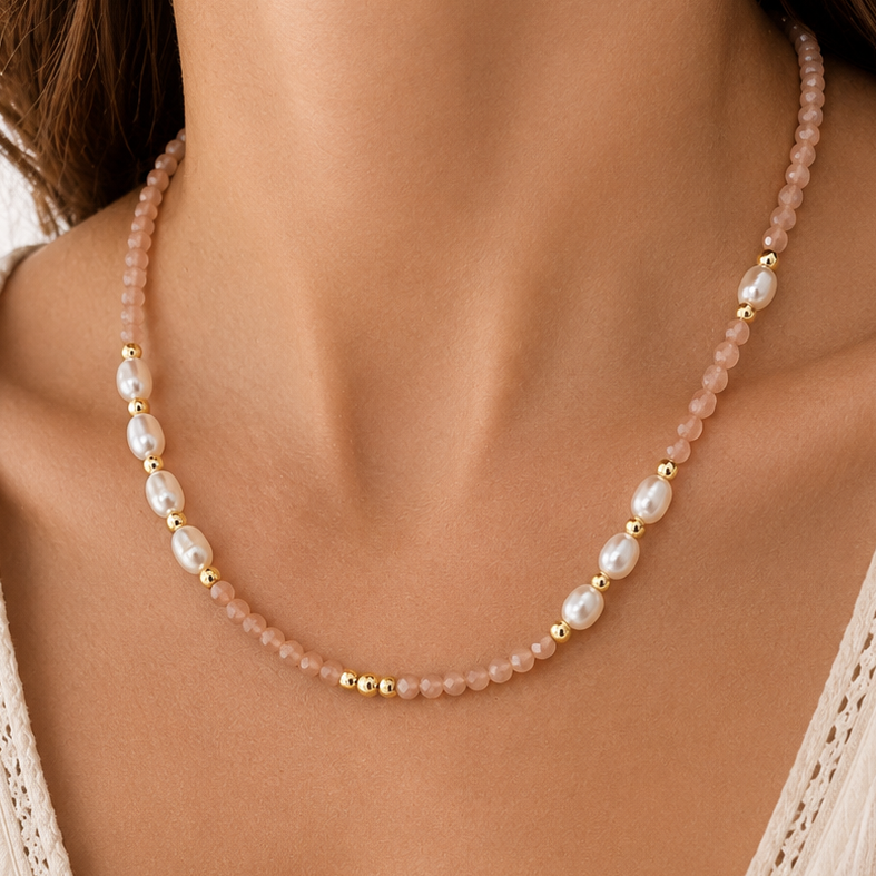 A close-up of a model wearing a delicate necklace made of pale sunstone beads, white pearls, and small gold spacer beads, paired with a cream-colored lace-trimmed top.