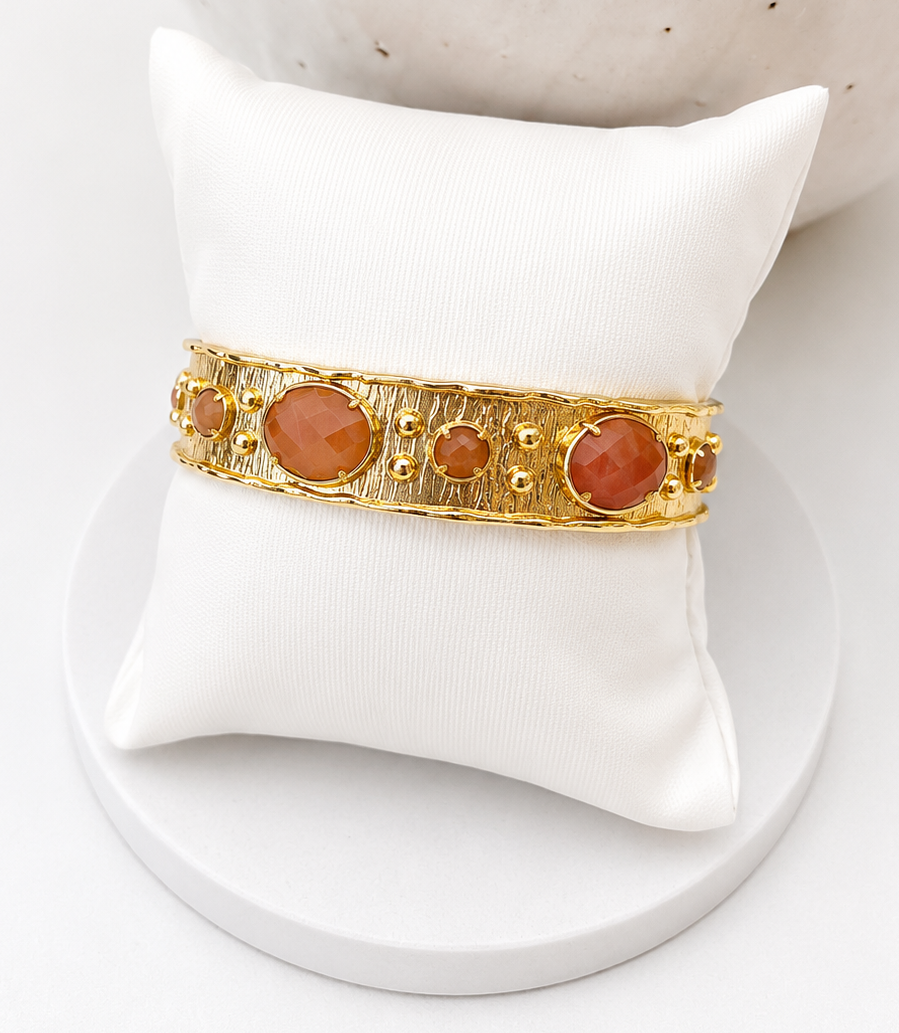 
                  
                    Gold bracelet with sunstone gemstone on a white stand against a white background
                  
                