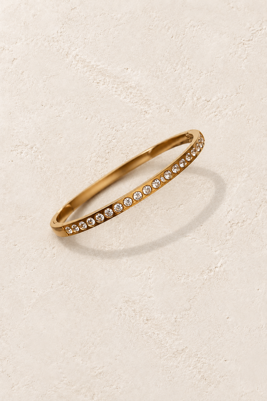 
                  
                    Amara Gold Round Crystal Bangle on cream beige textured background
                  
                
