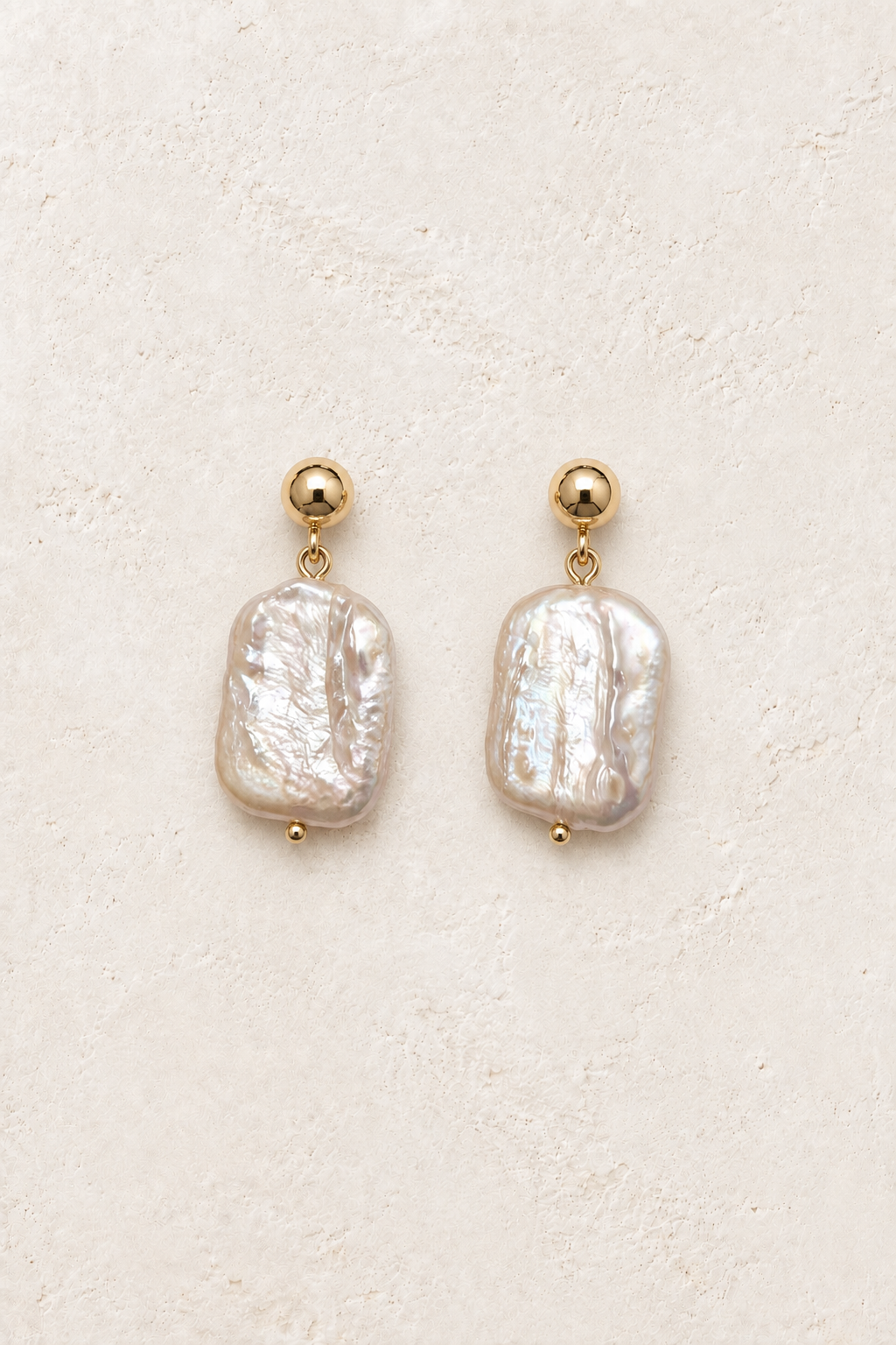 Aureva Baroque Pearl Drop Earrings on warm ivory textured background